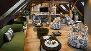 A modern loft-style living space with a high ceiling, exposed wooden beams, and a kitchen area in the background. - Small Luxury Hotel Ambassador Zürich (Zürich)