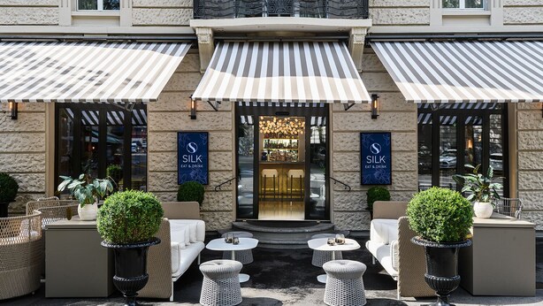 A restaurant with outdoor seating, a stone facade, and striped awnings. - Small Luxury Hotel Ambassador Zürich (Zürich)