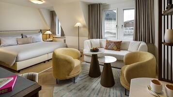 Ein Hotelzimmer mit einem Bett, einem Schlafsofa, zwei Sesseln, einem Couchtisch und einem Esstisch mit einem Buch und einer Obstschale.