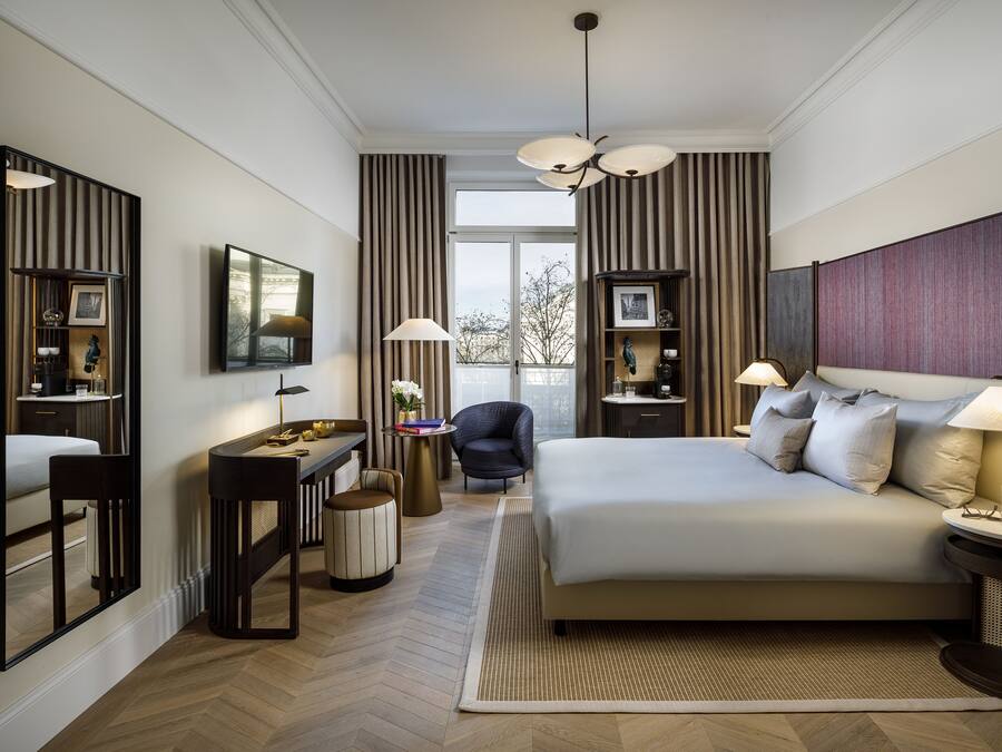 Una habitación de hotel moderna con una cama grande, un escritorio con una silla, un televisor y una ventana con cortinas.