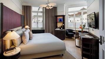 Ein Hotelzimmer mit einem großen Bett, Nachttischen, einem Schreibtisch, einem Sessel und einem Fernseher.