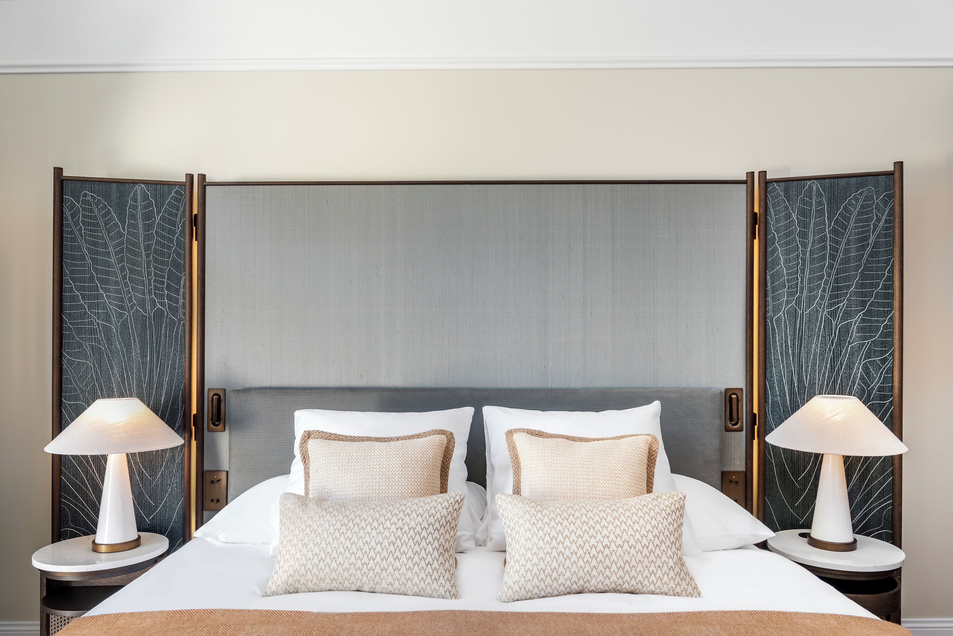 Una habitación de hotel con una cama grande, dos mesitas de noche con lámparas y un cabecero decorativo.