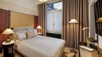 A hotel room with a large bed, two bedside lamps, a nightstand with a book, a small table, and a chair.
