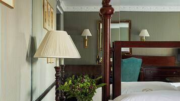 A hotel room with a bed, a nightstand with a lamp, a vase with flowers, and a mirror on the wall.