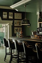 Eine Bar mit einer dunkelgrünen Wand, gerahmten Kunstwerken und einer hängenden Leuchte.
