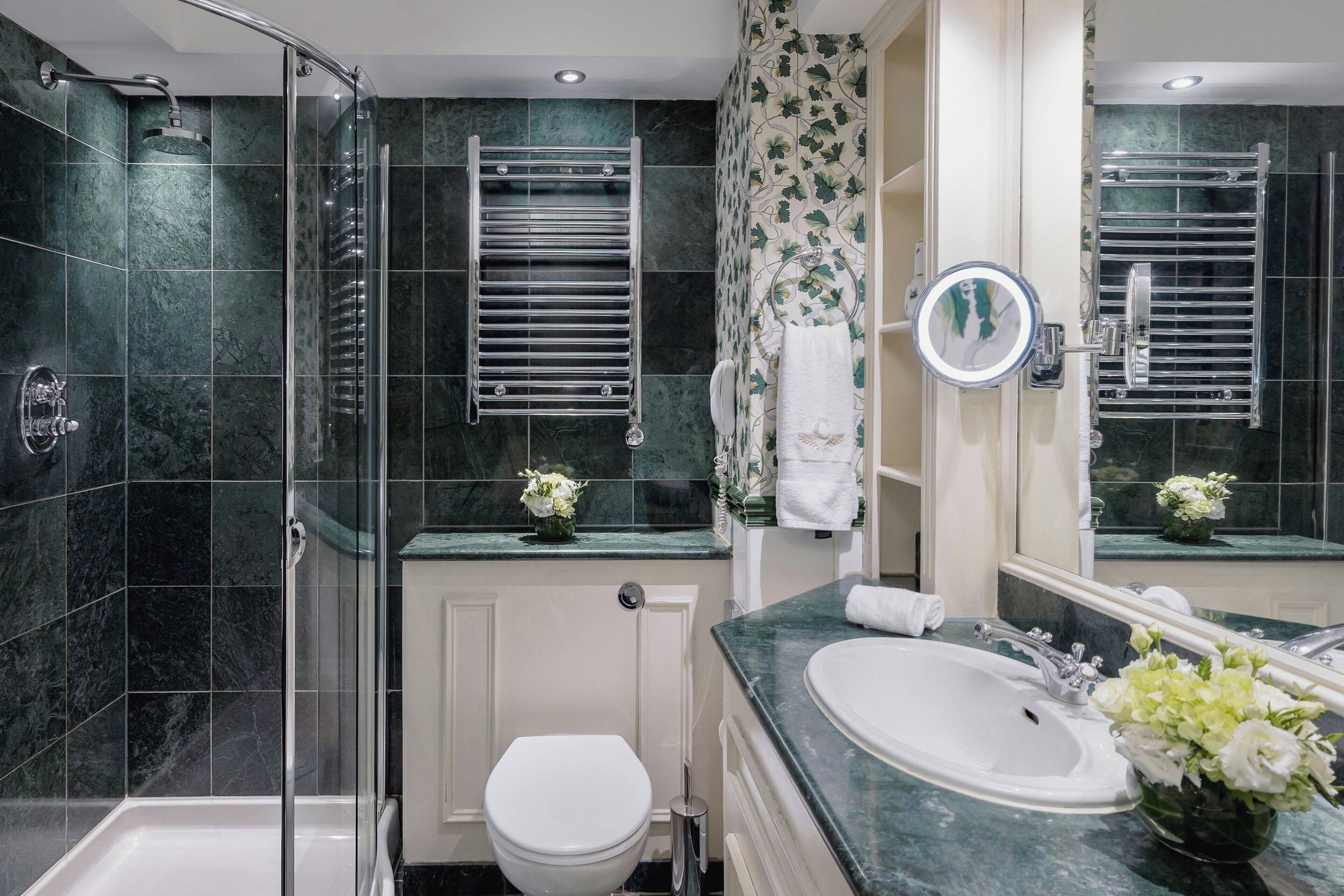 Un baño moderno con ducha de vidrio, inodoro blanco, lavabo con espejo y un florero con flores.