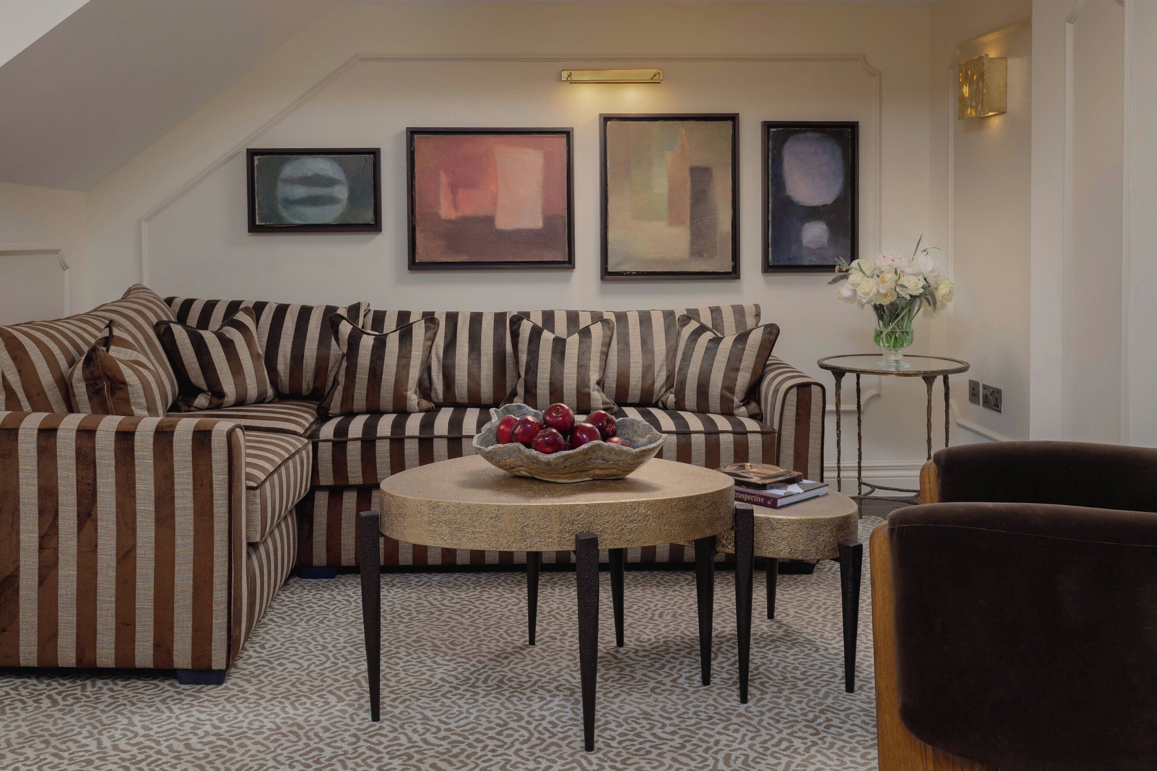 A living room with a striped sofa, a round coffee table with a bowl of fruit, and framed artwork on the wall.