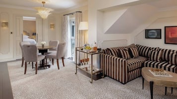Una sala de estar con un sofá a rayas, una mesa de comedor con sillas, un candelabro y vistas al dormitorio.