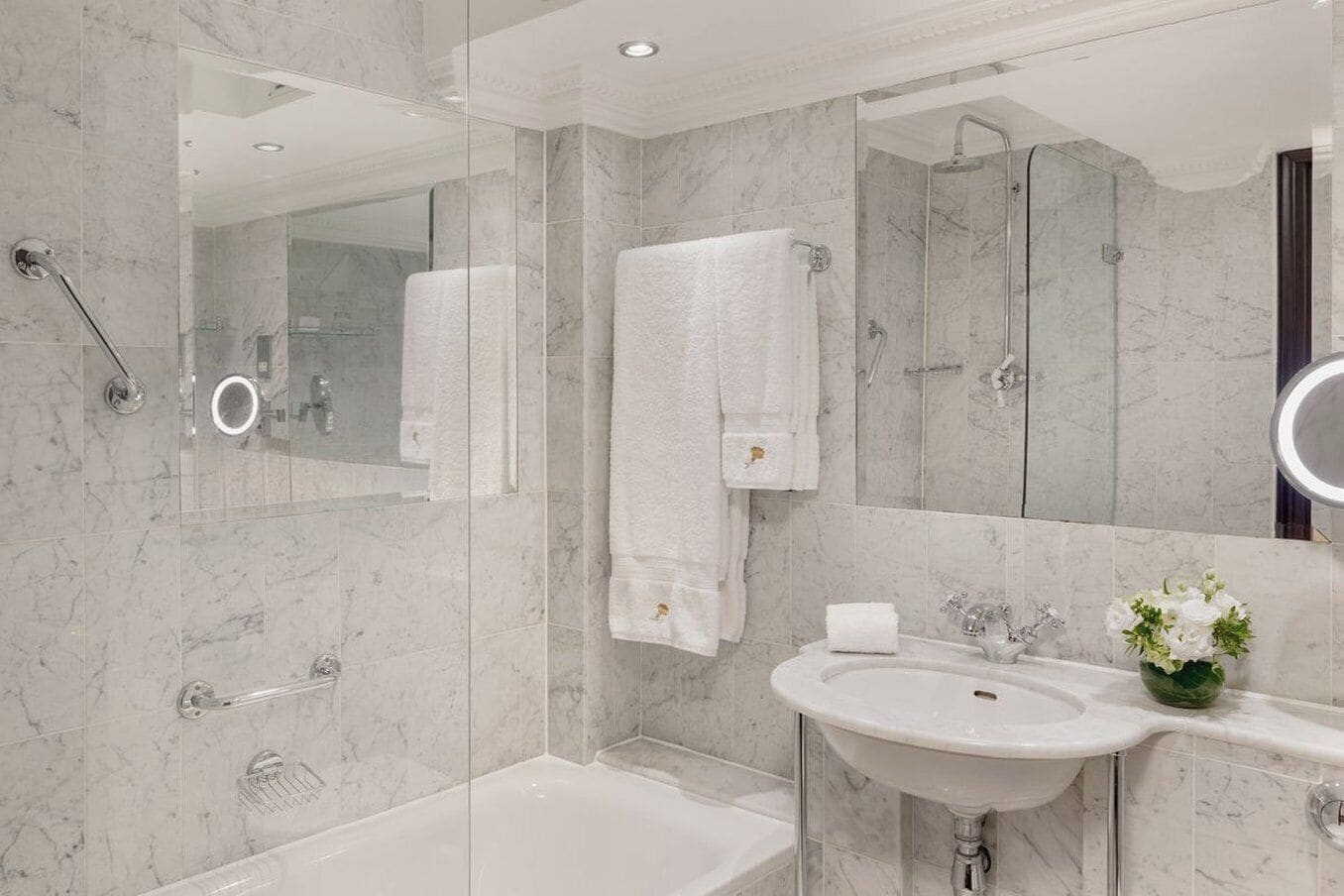Ein modernes Badezimmer mit einer Glaskabine zur Dusche, einer Badewanne, einem Waschbecken mit Spiegel und einer Vase mit Blumen.