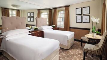 A hotel room with two beds, a sitting area with a chair, a small table, and a potted plant.