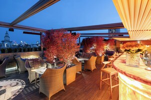 An outdoor seating area with wicker furniture, a bar counter, and a view of the city skyline.