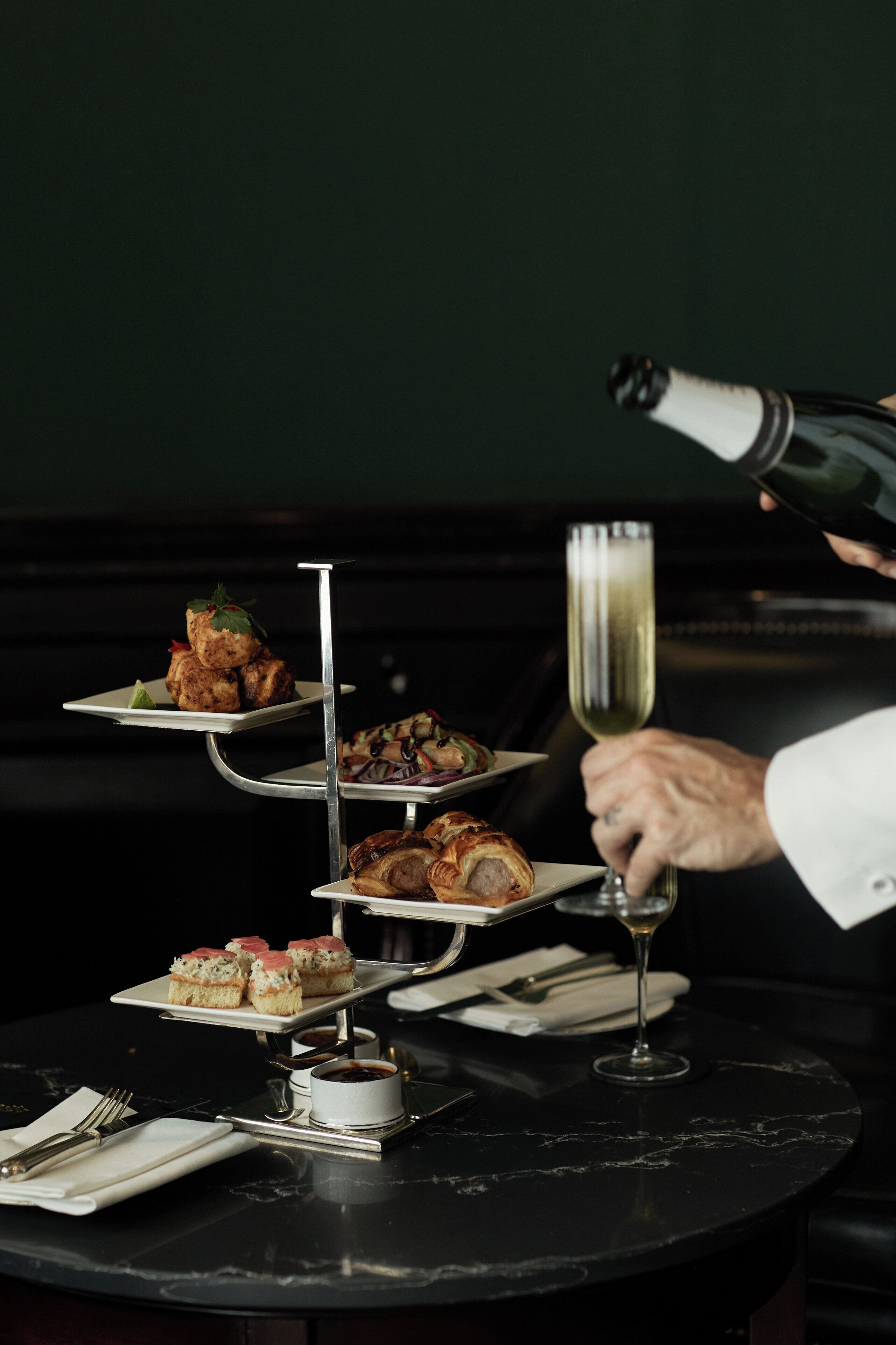 A three-tiered dessert stand with various pastries and a glass of champagne on a table.