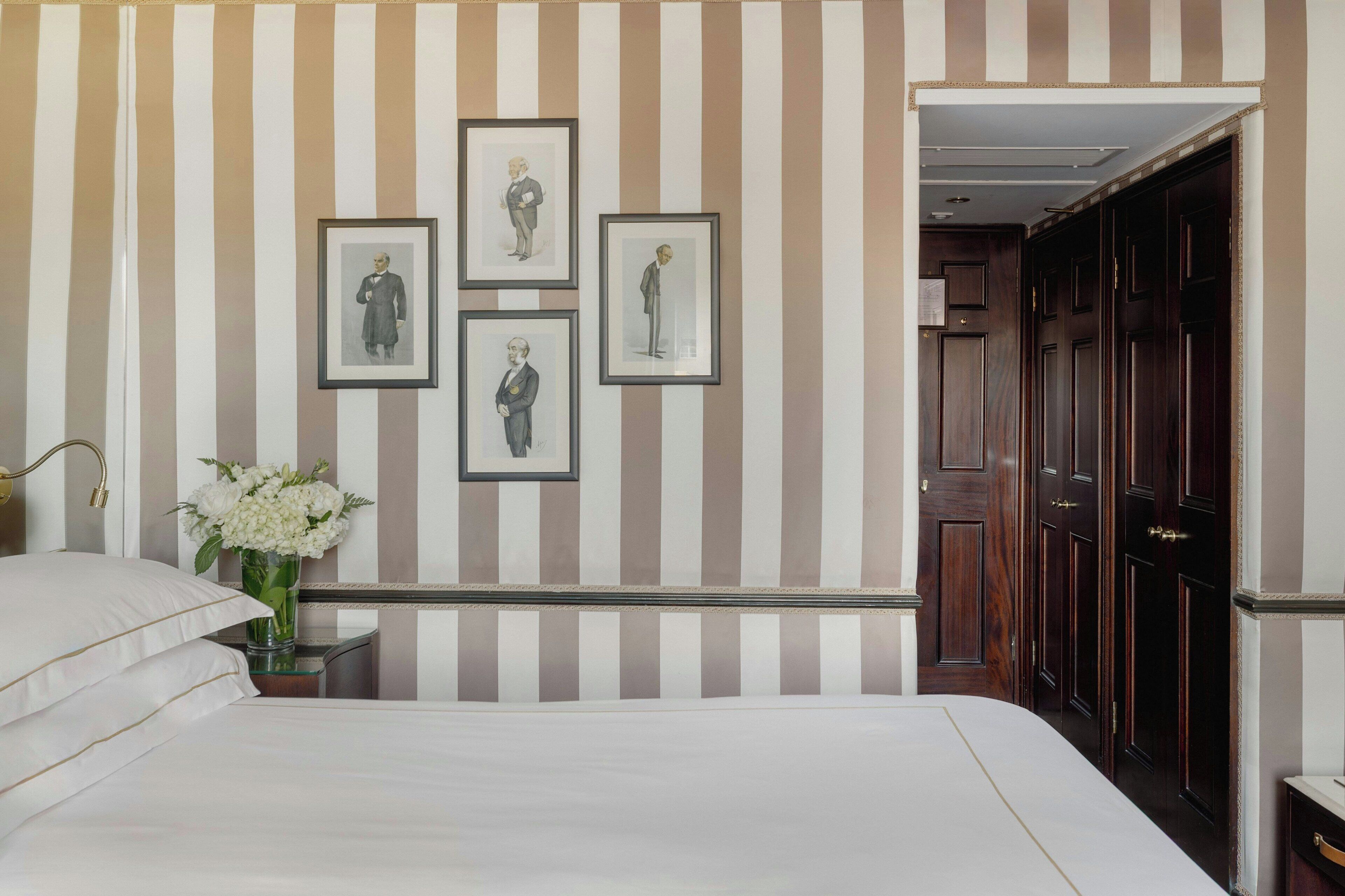 A hotel room with a striped wall, framed pictures, a vase of flowers, and a wooden wardrobe.