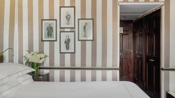 A hotel room with a striped wall, framed pictures, a vase of flowers, and a wooden wardrobe.