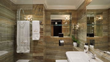 A bathroom with marble walls, a glass shower enclosure, a white sink, and a large mirror.