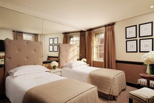 Ein Hotelzimmer mit zwei Betten, einem Schreibtisch, einem Stuhl, einem Fernseher und gerahmten Bildern an der Wand.