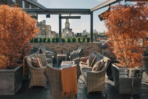 A rooftop patio with wicker furniture, a view of a cityscape, and a stone wall.