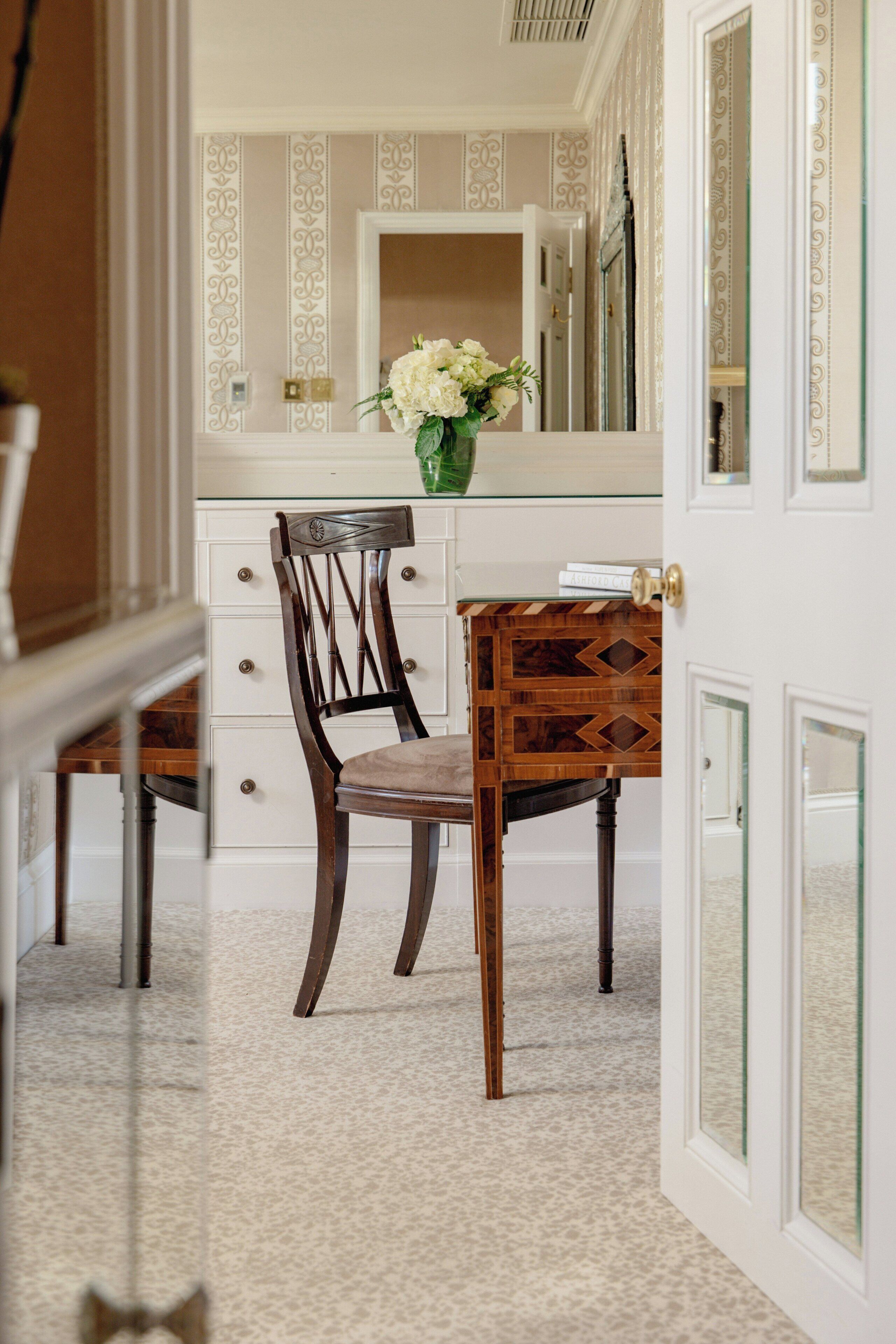 A room with a wooden chair, a small table, and a vase with flowers.