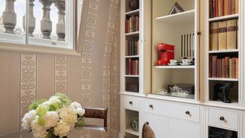 Una stanza con un tavolo da pranzo, sedie, un vaso di fiori, una libreria e una finestra con ringhiera.