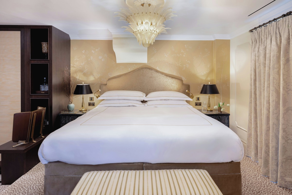 A large bed with a headboard, two bedside tables with lamps, a small cabinet, and a patterned carpet.