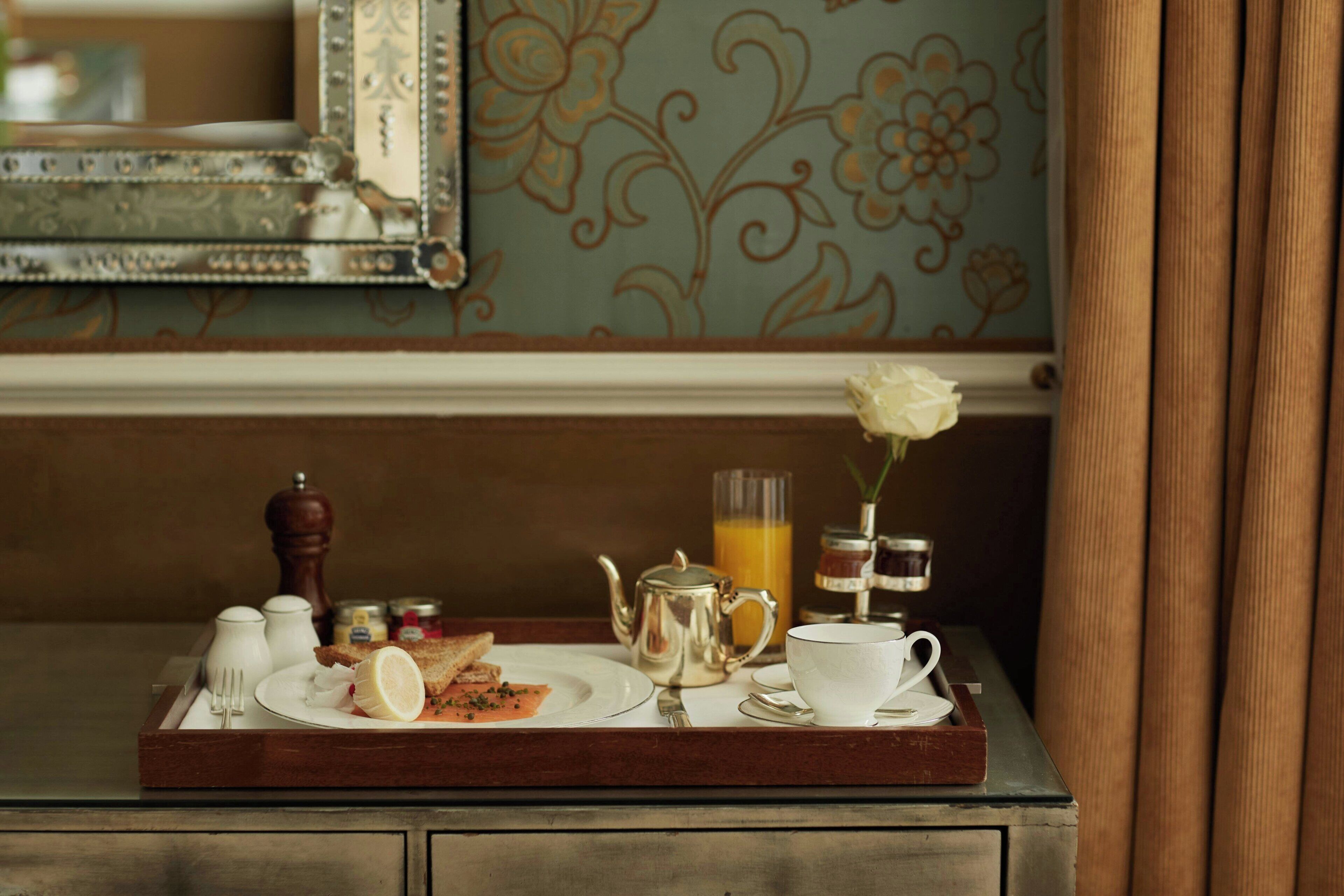 Un plateau de petit-déjeuner avec des toasts, un citron, une théière, une tasse et un verre de jus d’orange, posé sur une table en bois.