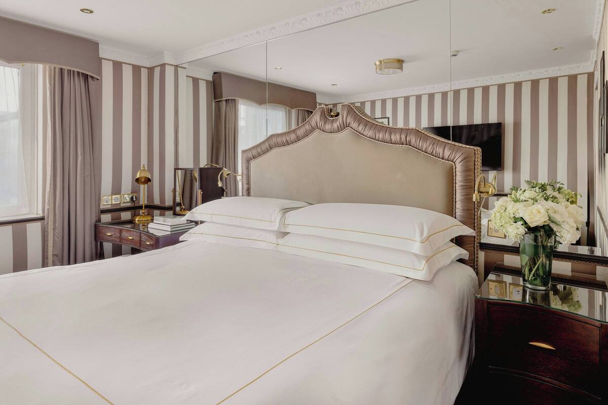 A large bed with a tufted headboard, a bedside table with a lamp, and a vase with flowers.