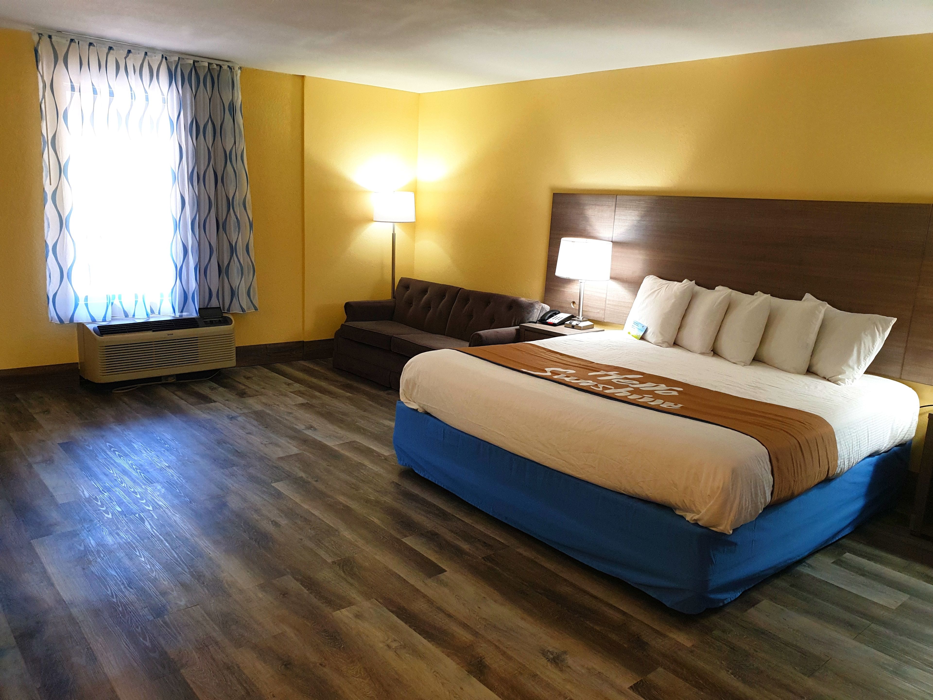 Una habitación de hotel con cama, sofá, mesita de noche con lámpara y equipo de aire acondicionado.