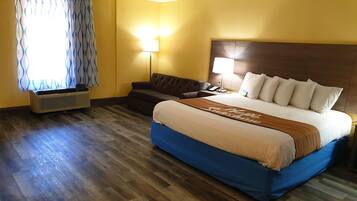 Una habitación de hotel con cama, sofá, mesita de noche con lámpara y equipo de aire acondicionado.