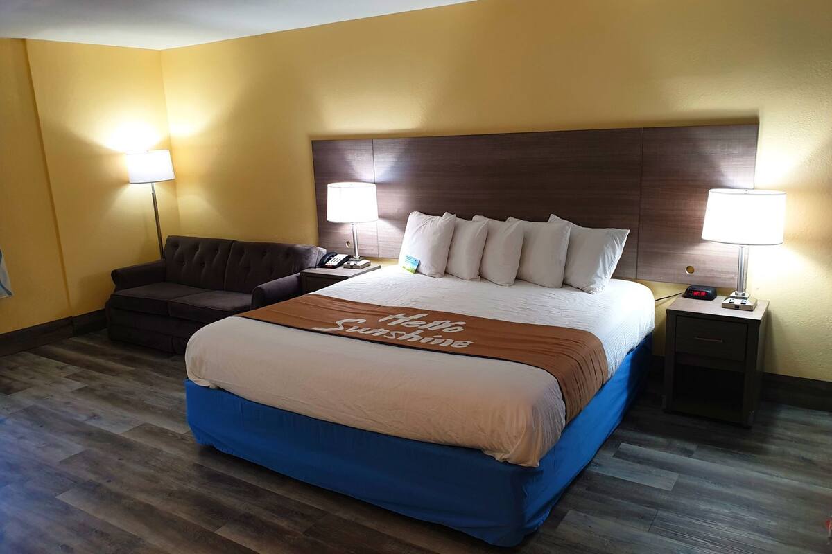 A hotel room with a large bed, two bedside lamps, a sofa, and a nightstand with a phone and alarm clock.