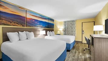 A hotel room with two beds, a desk, a lamp, and a large landscape painting on the wall.