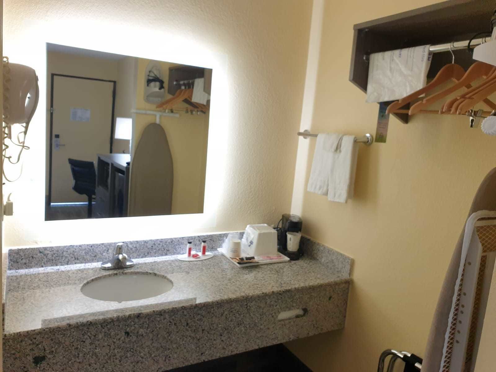 A bathroom with a granite countertop, a sink, a mirror, a towel rack, and a shower area.
