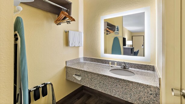 A bathroom with a granite countertop sink, a large mirror, a towel rack with hangers, and a towel on the wall.