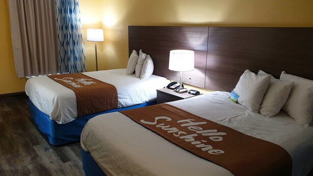 A hotel room with two beds, a nightstand with a lamp, and a view of the outside through curtains. - Days Inn by Wyndham Cleveland TN (Cleveland)