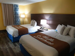 Une chambre d’hôtel avec deux lits, une table de chevet avec une lampe et une vue sur l’extérieur à travers les rideaux.
