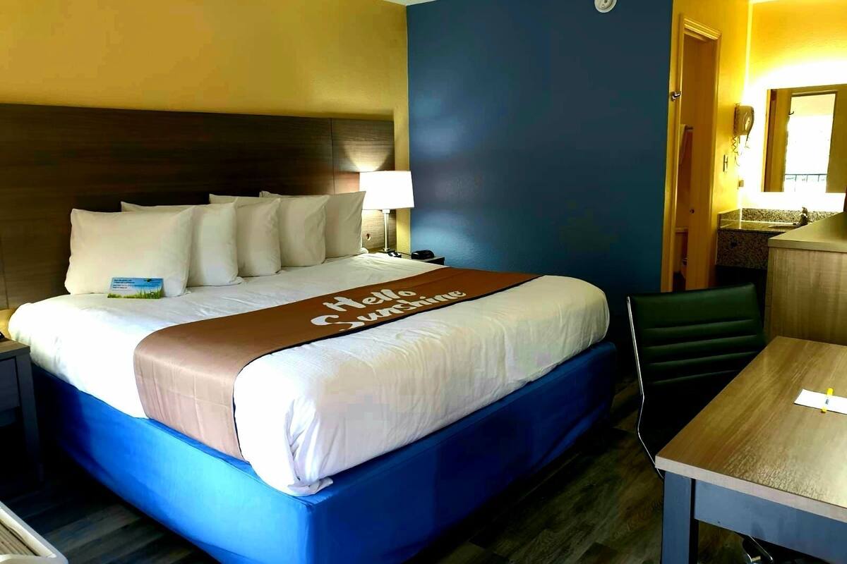 A hotel room with a bed, a desk, a chair, and a bathroom visible through an open door.