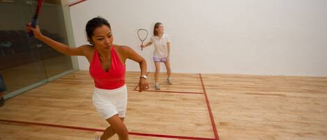 A squash court with wooden flooring and red boundary lines.