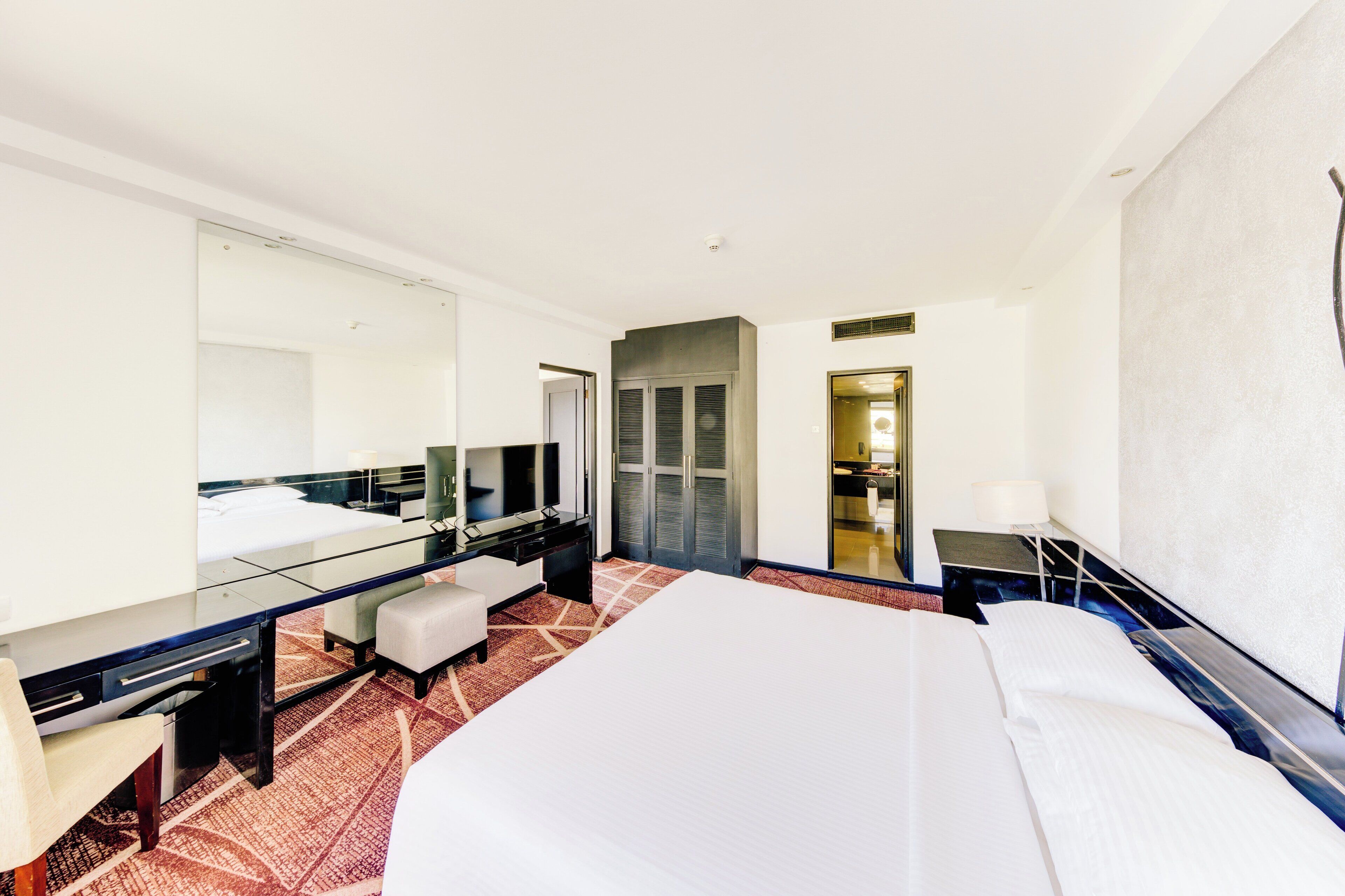 Una habitación de hotel con una cama grande, un escritorio, una silla, un espejo y un armario.