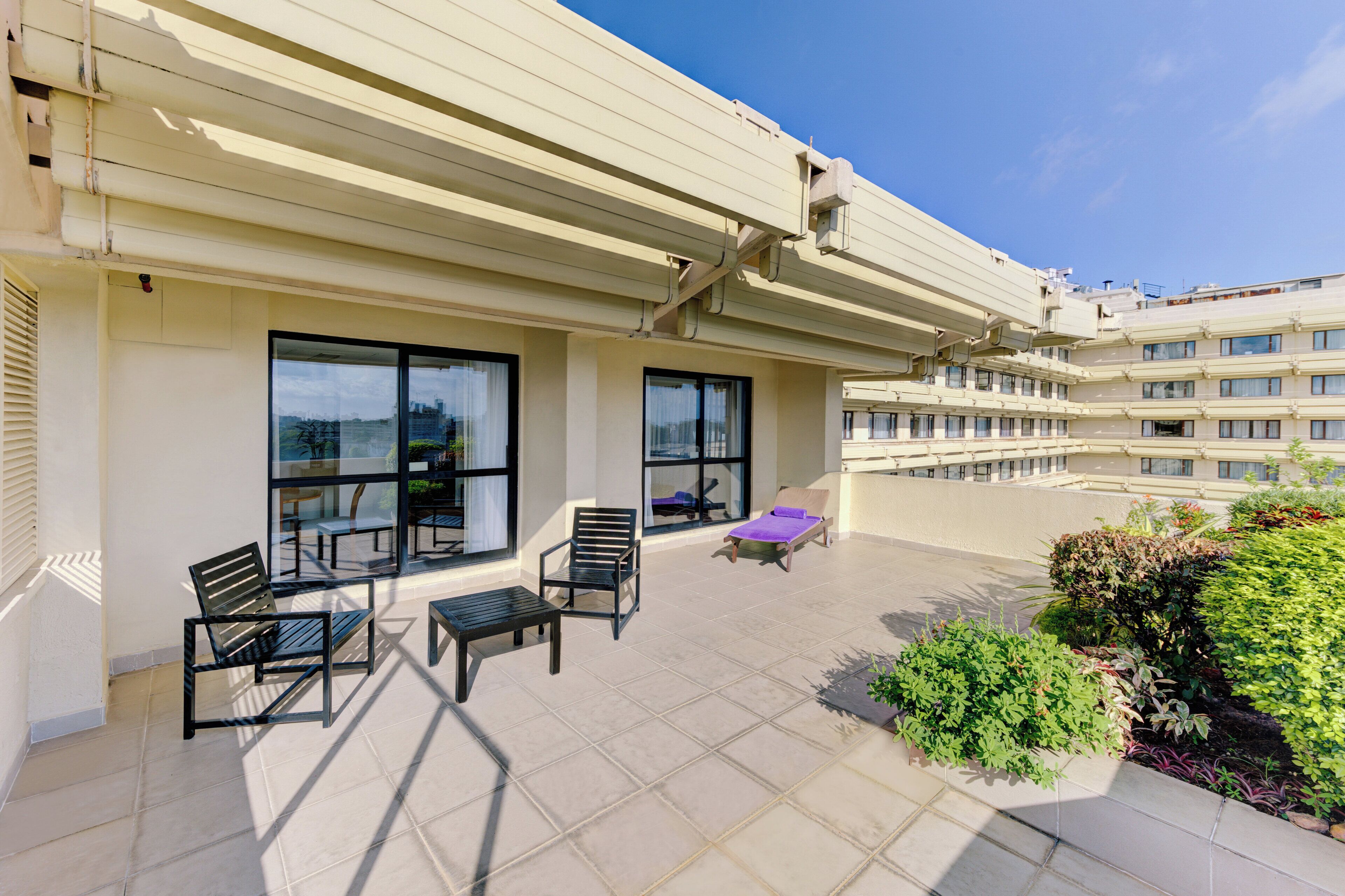 Un balcon d’hôtel avec des sièges d’extérieur, de grandes fenêtres et une vue sur la ville.