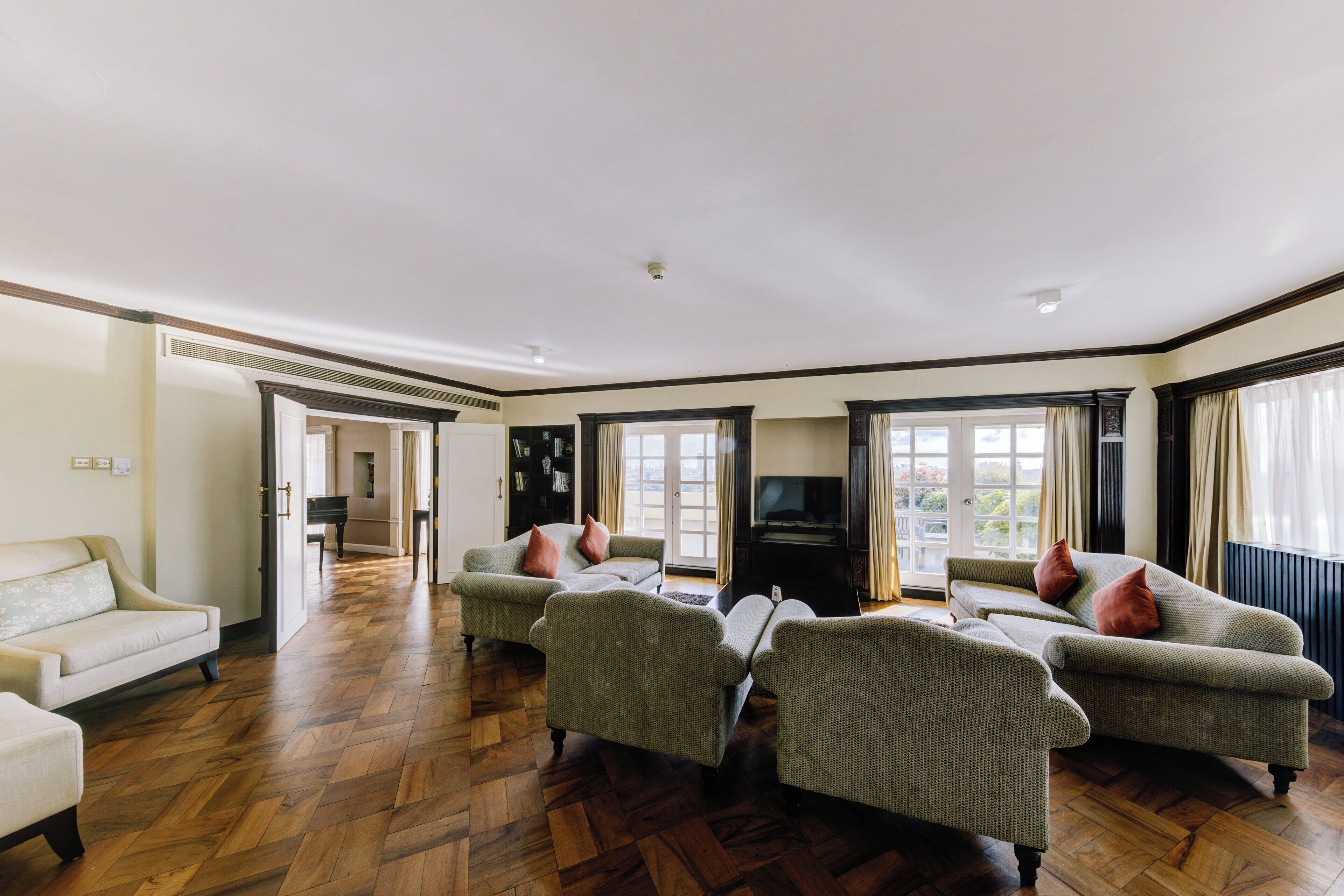 A spacious living room with a wooden parquet floor, a sofa set, a television, and a piano.