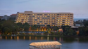 Un hotel grande con varios pisos y balcones, una barcaza flotante en primer plano y una masa de agua al fondo.