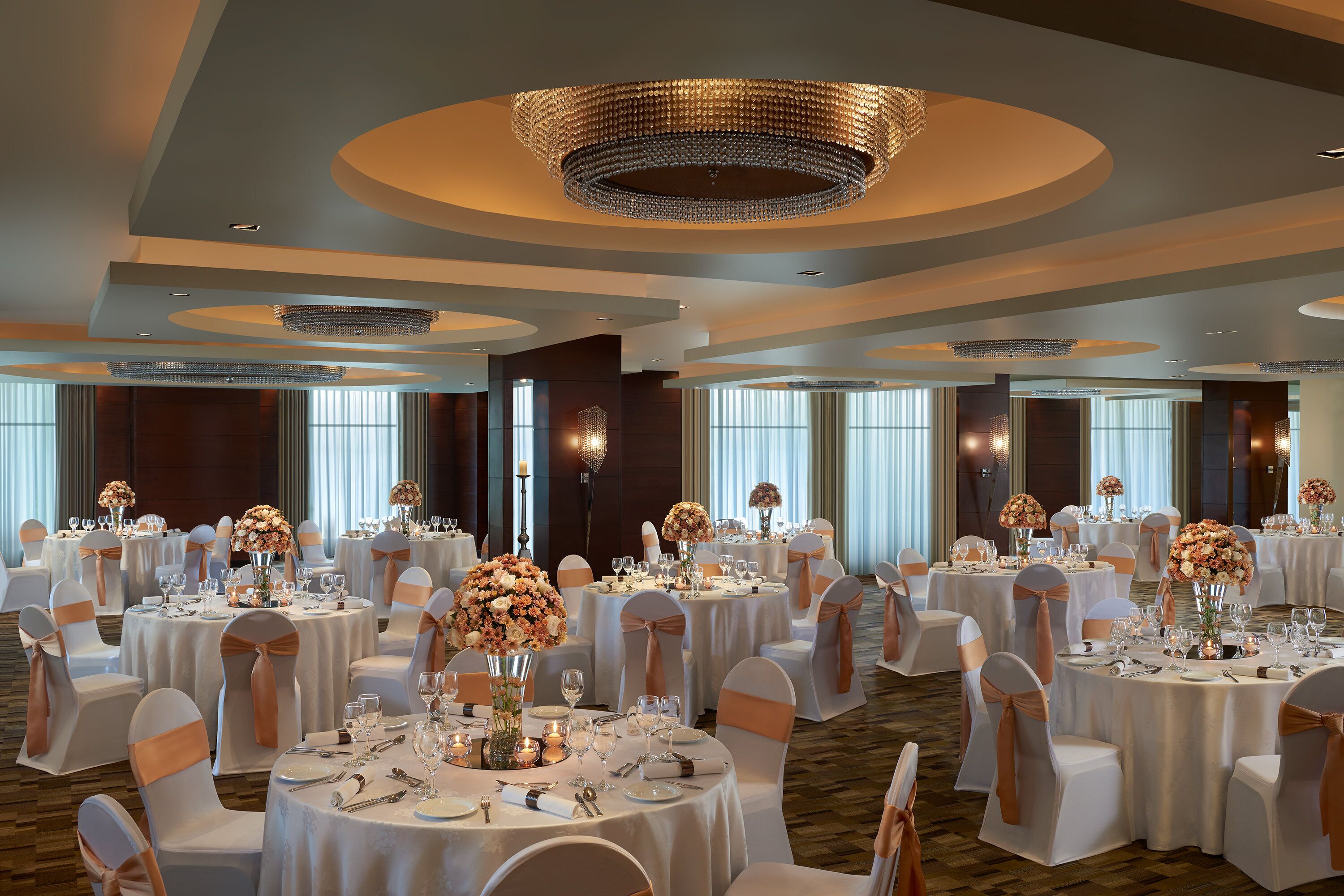 Un salón de banquetes con mesas redondas, manteles blancos y centros de mesa florales.