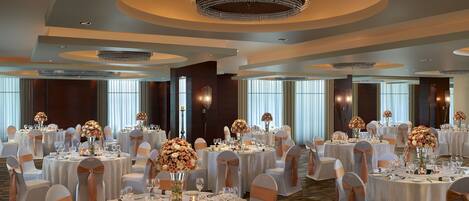 Un salón de banquetes con mesas redondas, manteles blancos y centros de mesa florales.