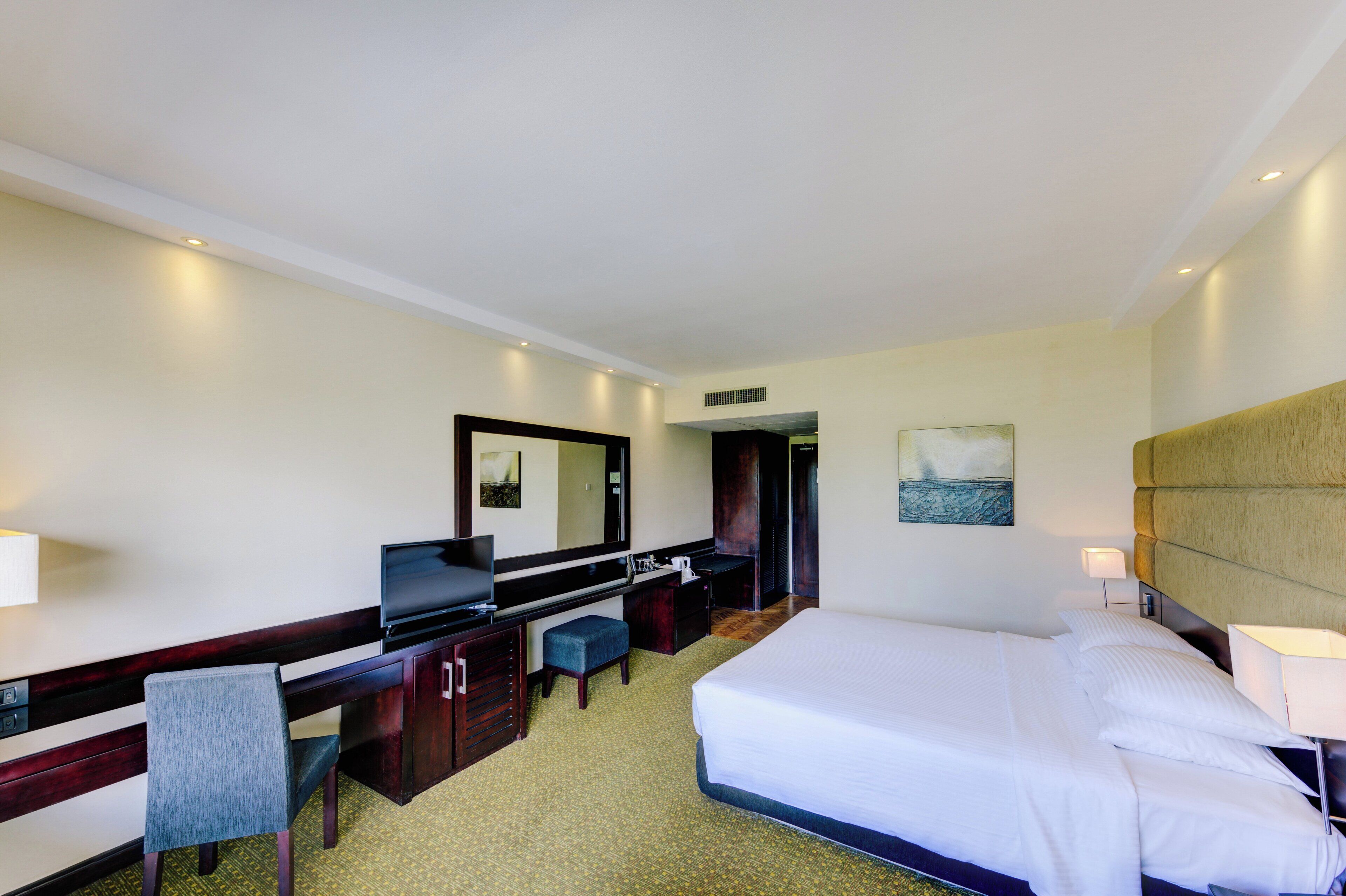 A hotel room with a bed, a desk, a chair, a television, a mirror, and a painting on the wall.