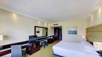Une chambre d’hôtel avec un lit, un bureau, une chaise, une télévision, un miroir et un tableau au mur.