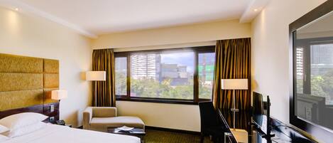 A hotel room with a large bed, a desk, a chair, a TV, and a window with curtains.