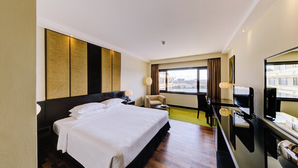 Een hotelkamer met een groot bed, een bureau met een computer, een stoel en uitzicht op de stad door het raam.