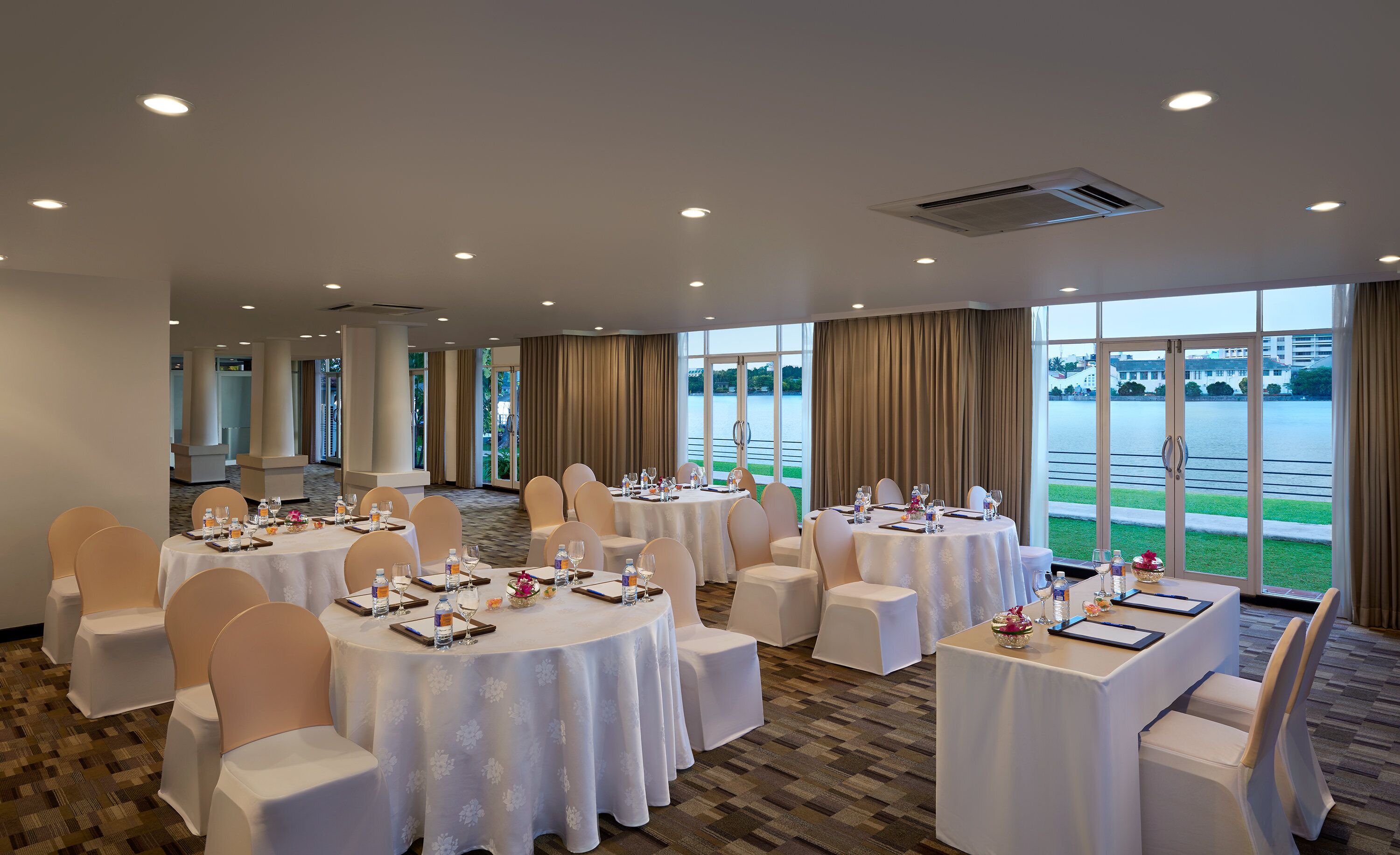 A conference room with round tables, white chairs, and a large window overlooking a body of water.