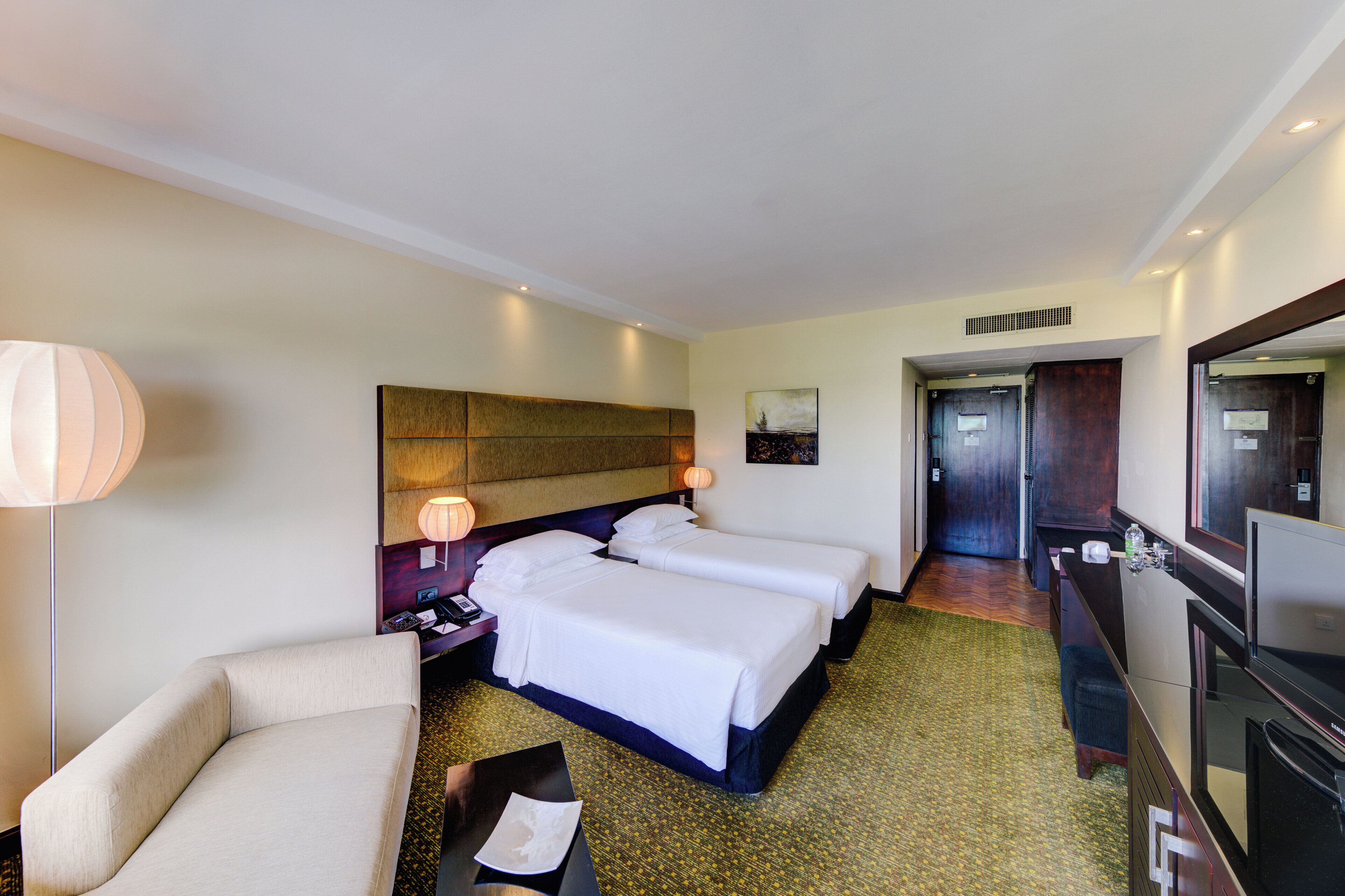 A hotel room with two beds, a sofa, a desk, a lamp, and a television.