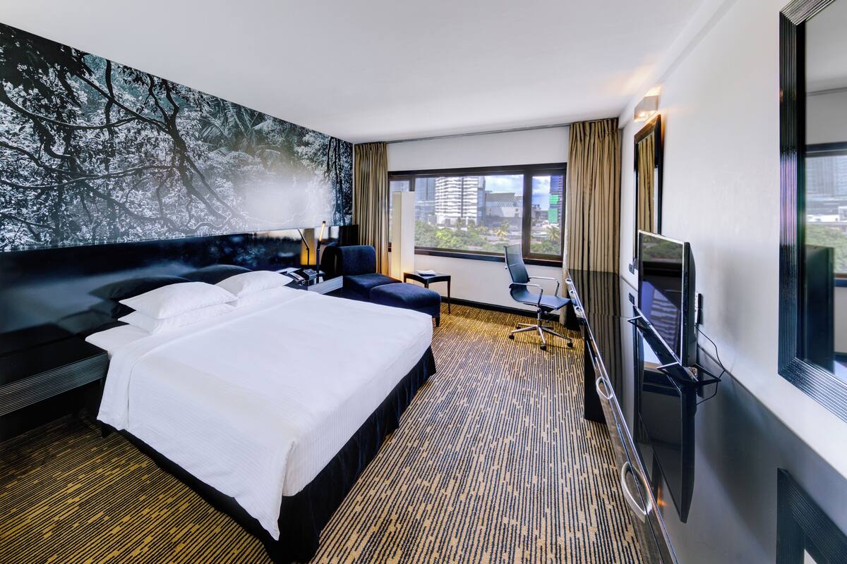Ein modernes Hotelzimmer mit einem großen Bett, einem Schreibtisch, einem Sessel und einem Fernseher.