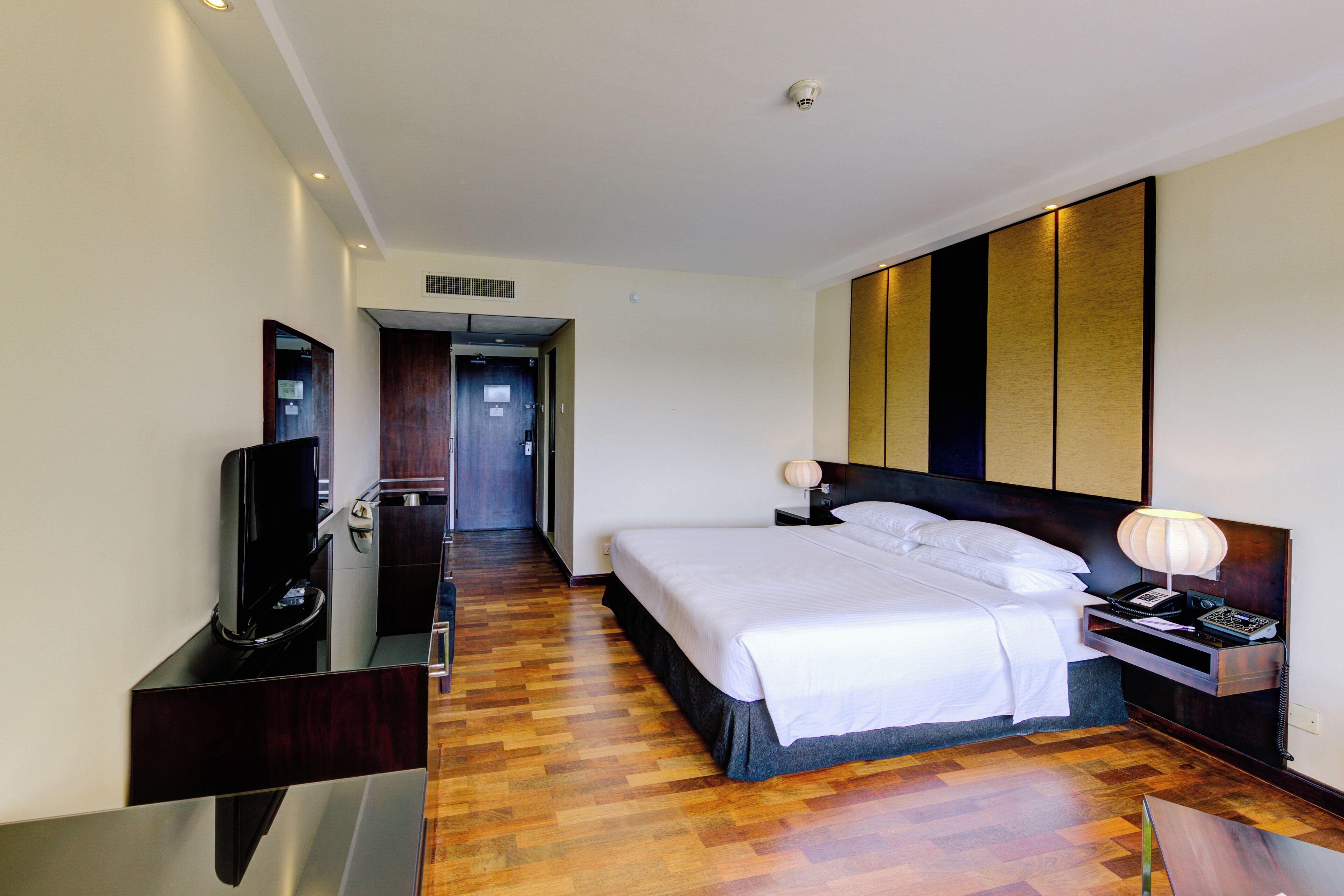 Une chambre d’hôtel avec un grand lit, un téléviseur posé sur un meuble, une table de chevet avec une lampe et un plancher en bois.